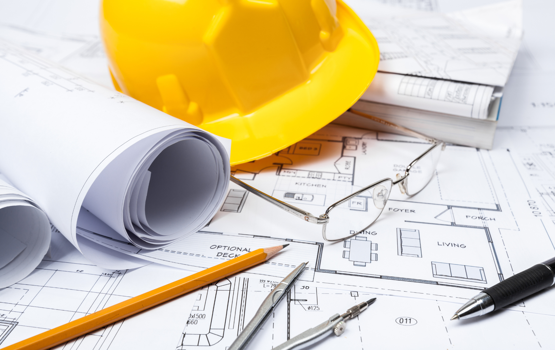 Yellow hard hat on architectural blueprints with pen, pencil, and glasses.