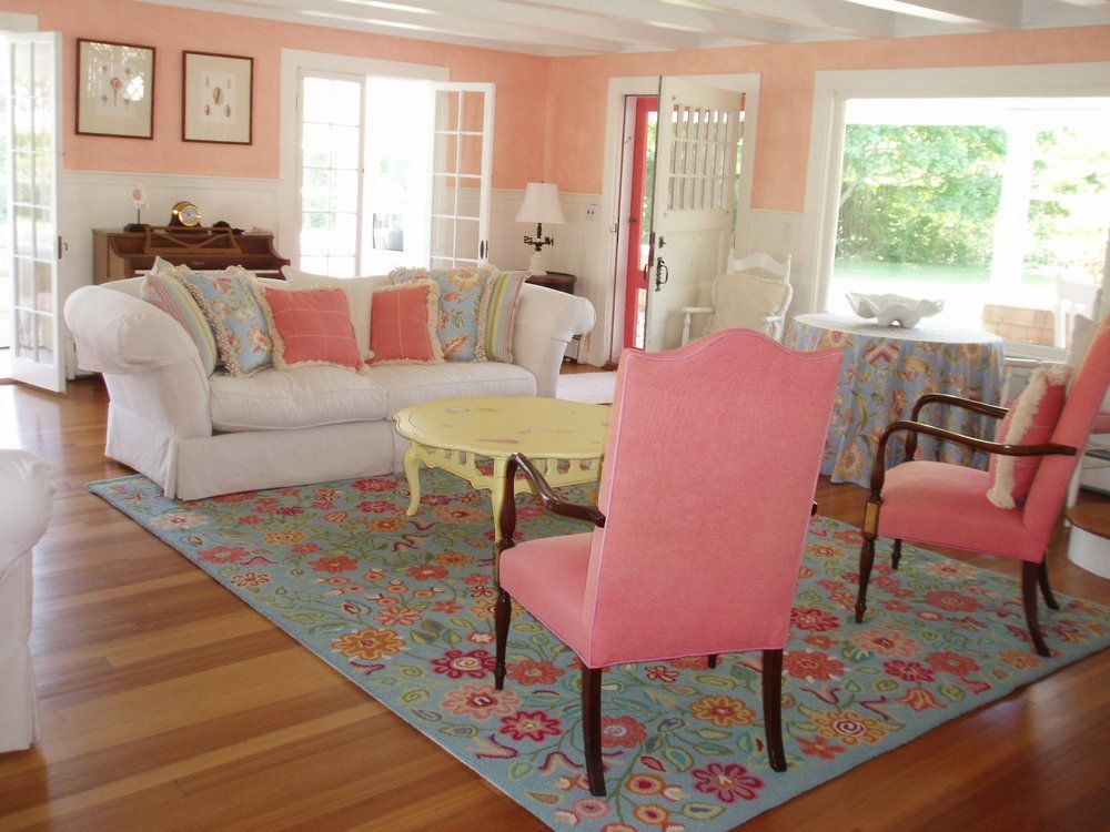 Living room with peach walls, white sofa, floral rug, and pink chairs.