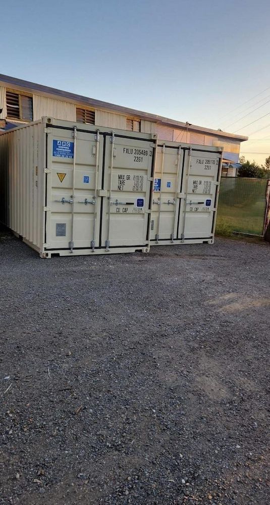 Three Beige Shipping Containers on Gravel With a Building in the Background — Gantic Removals & Storage in Tivoli, QLD