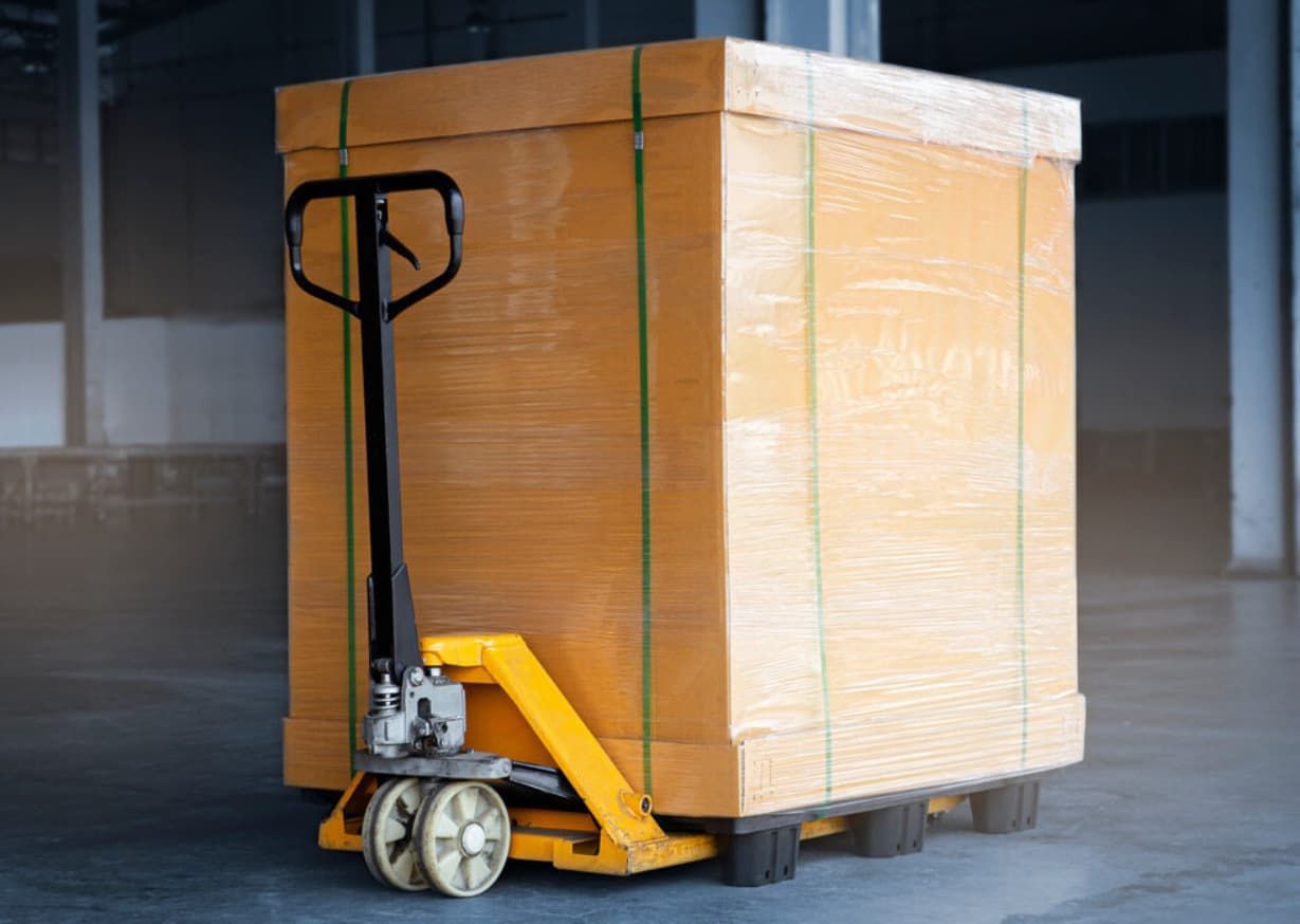 A Yellow Pallet Jack Lifting A Large Cardboard Box In A Warehouse — Gantic Removals & Storage in Brisbane, QLD