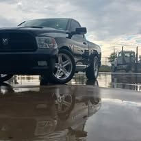 Black Dodge Ram truck parked on a wet surface; front view, silver wheels.