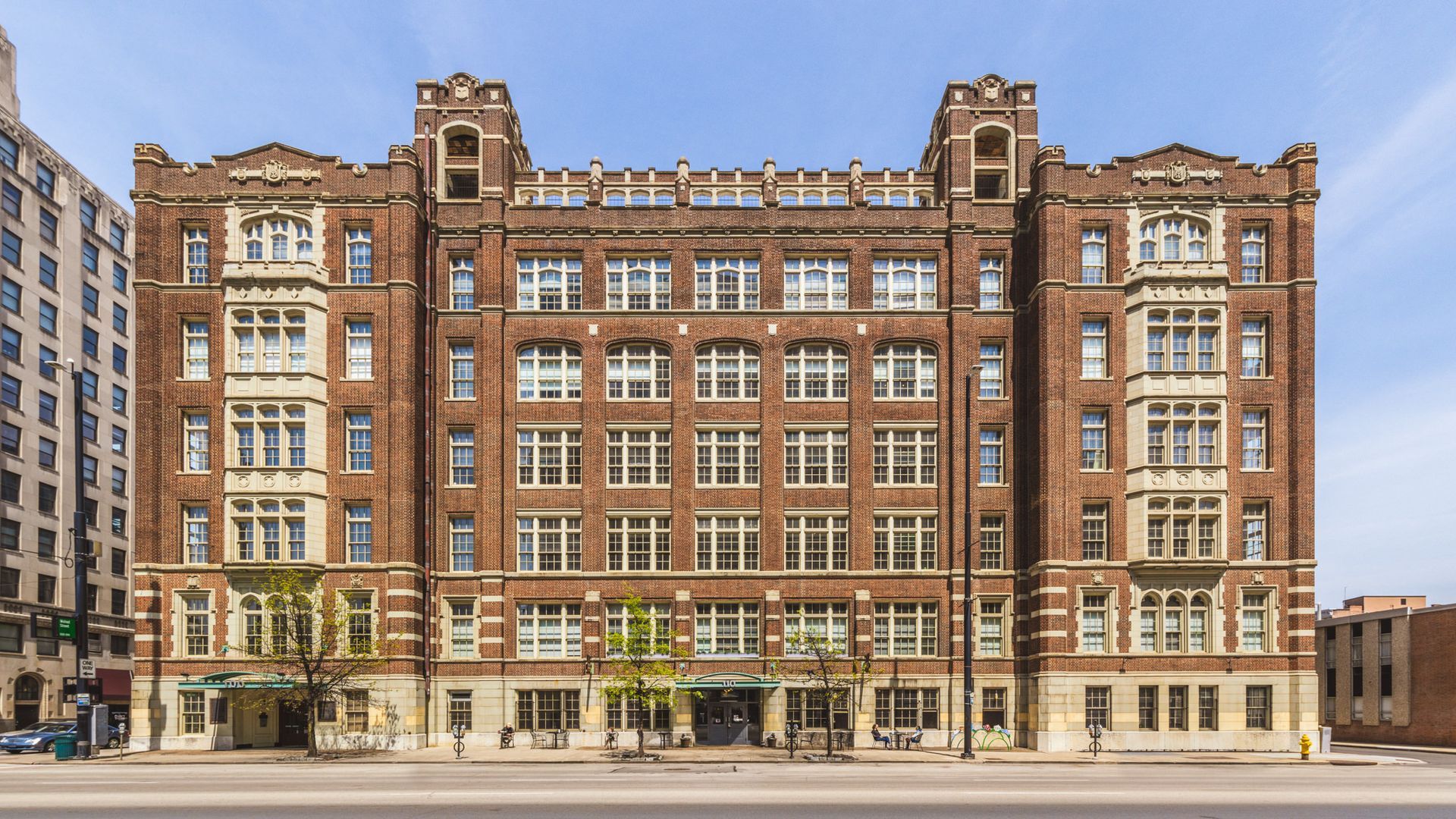 A large brick building with a lot of windows is sitting on the side of a city street.