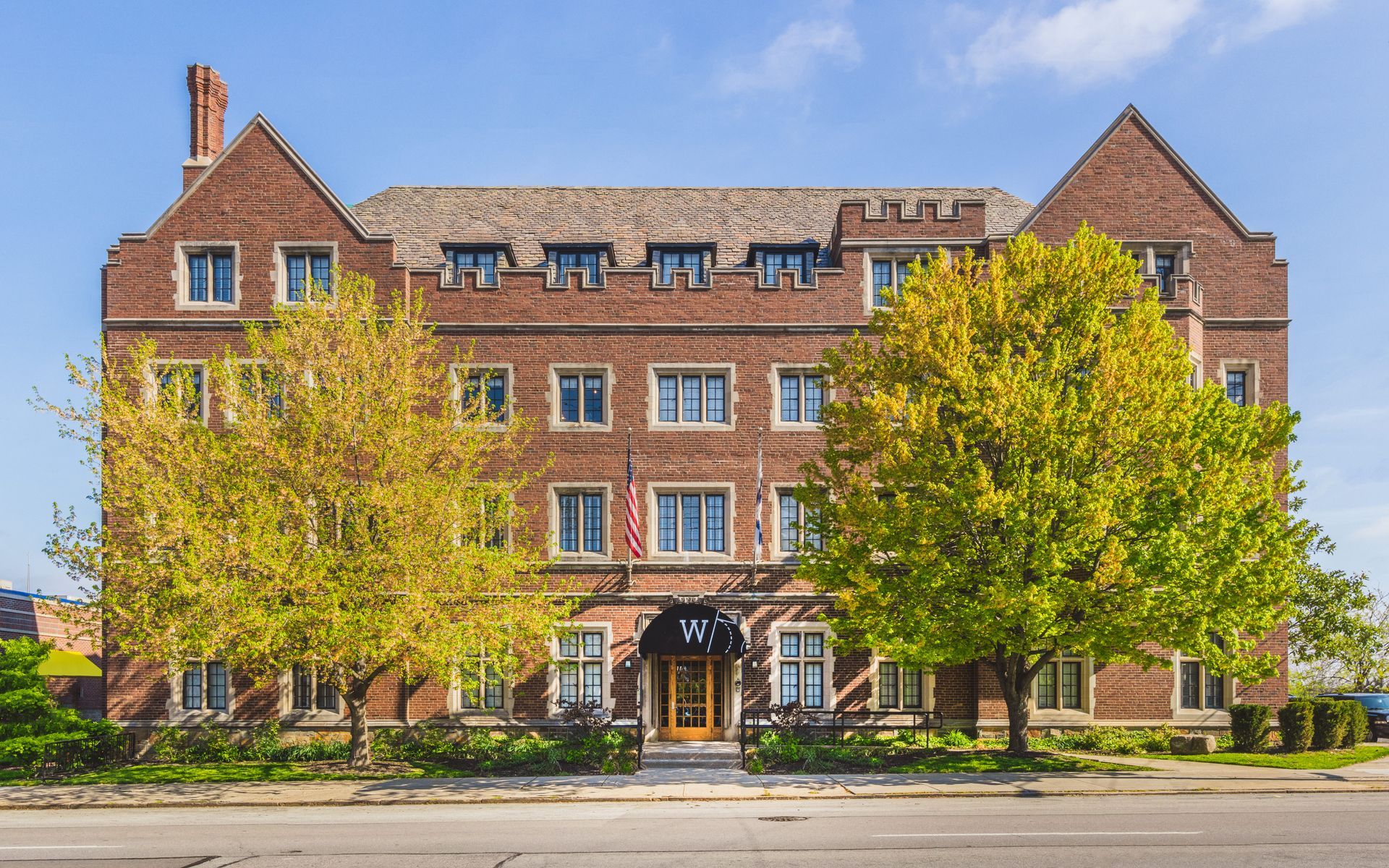 A large brick building with trees in front of it on a sunny day.