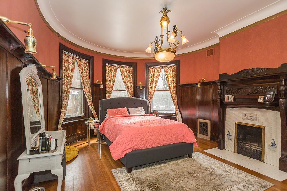 A bedroom with a bed , fireplace , dresser and mirror.