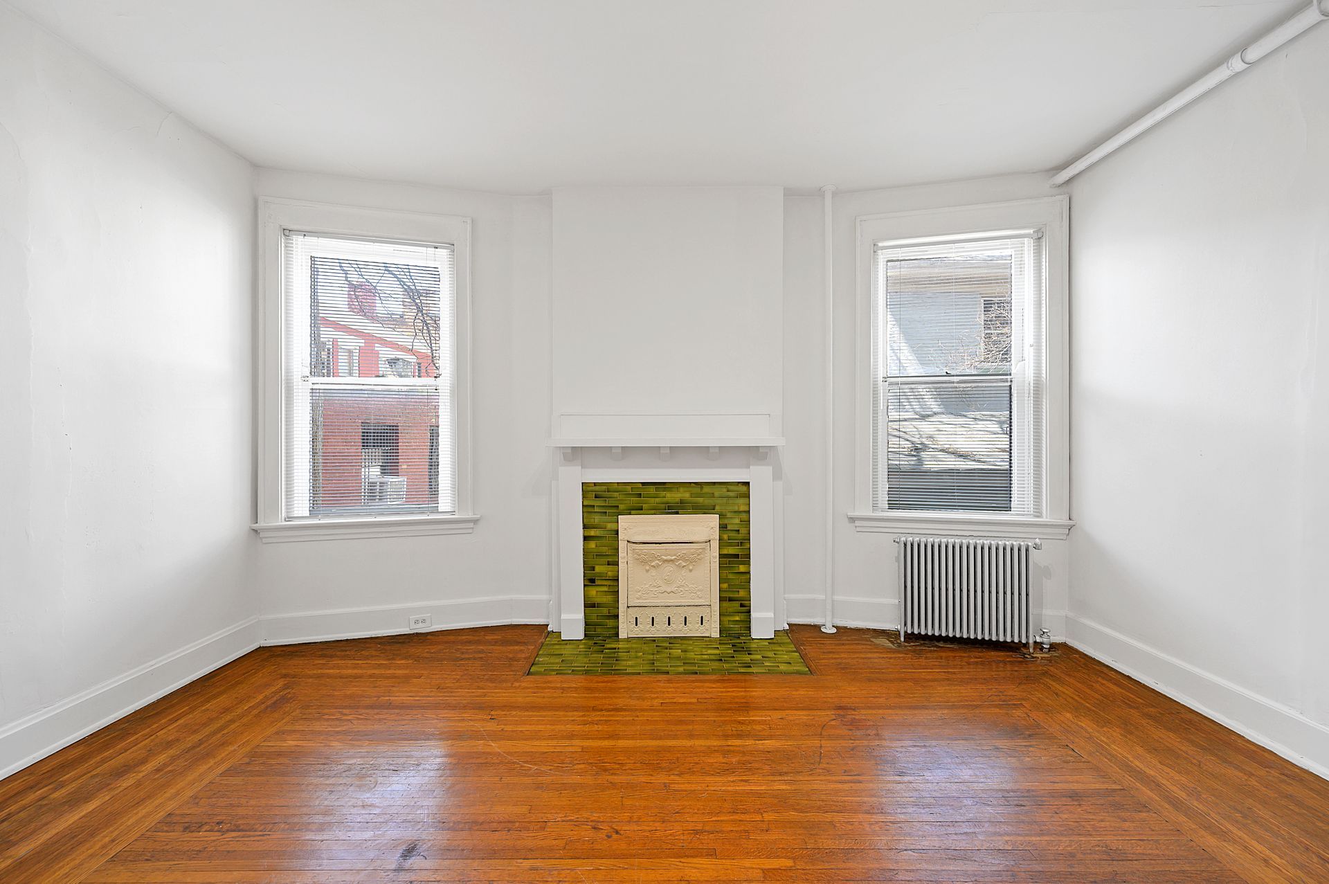 An empty living room with a fireplace and two windows.