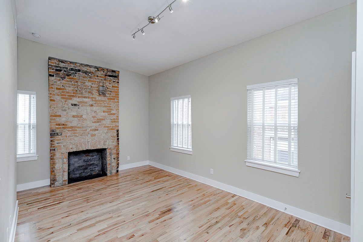 An empty living room with a fireplace and two windows.