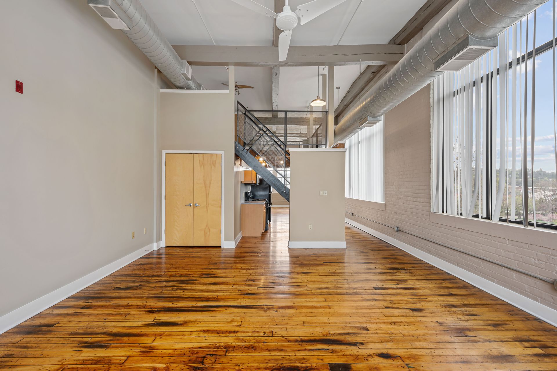 A large empty room with hardwood floors and a ceiling fan.