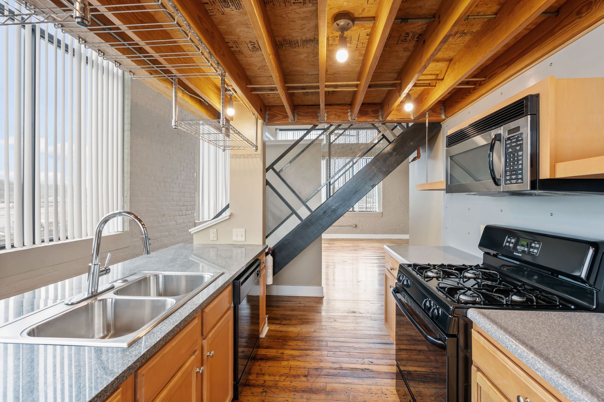 A kitchen with a sink , stove , microwave and stairs.