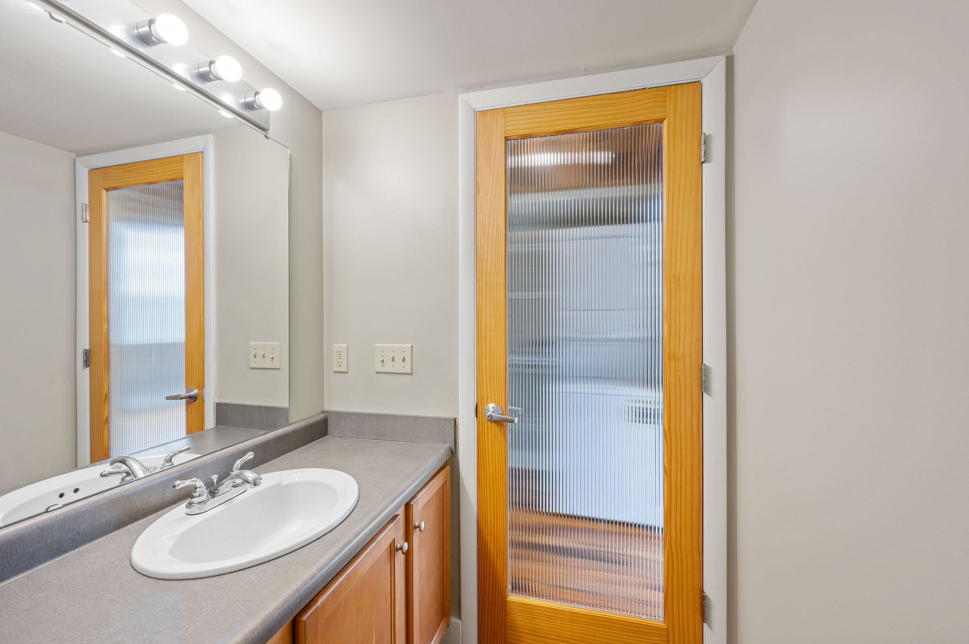 A bathroom with a sink , mirror and door.