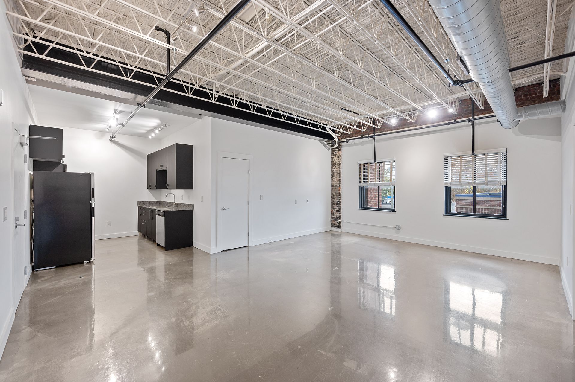 A large empty room with a kitchen in the background