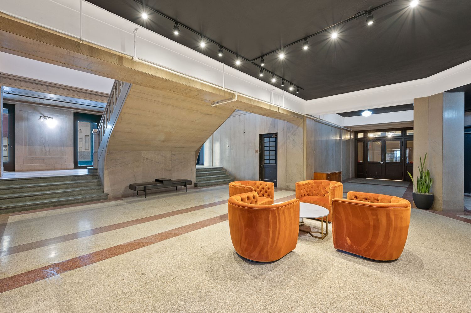 A lobby with orange chairs and a table in a building.