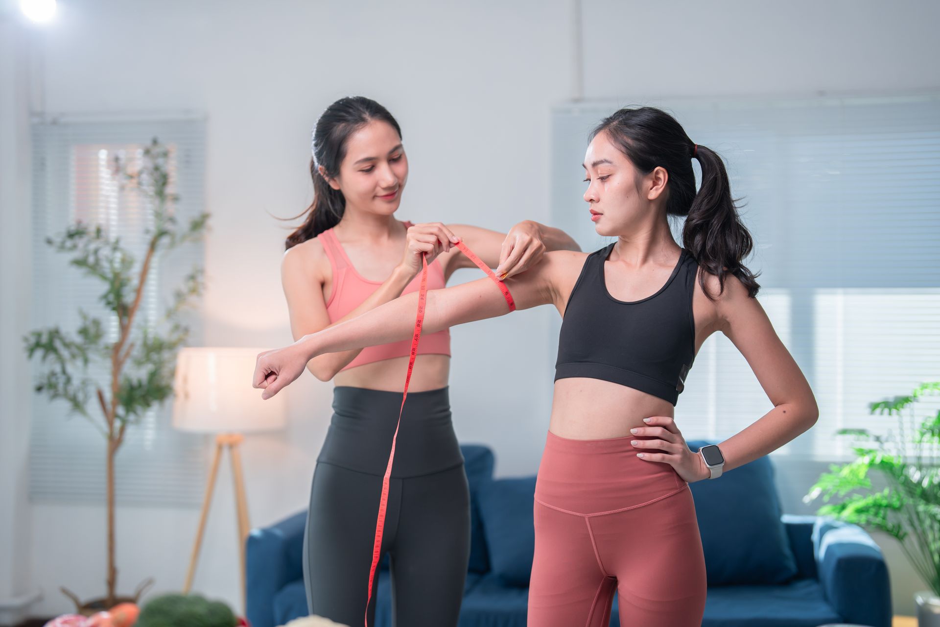 Two women are measuring each other 's arms with a tape measure.