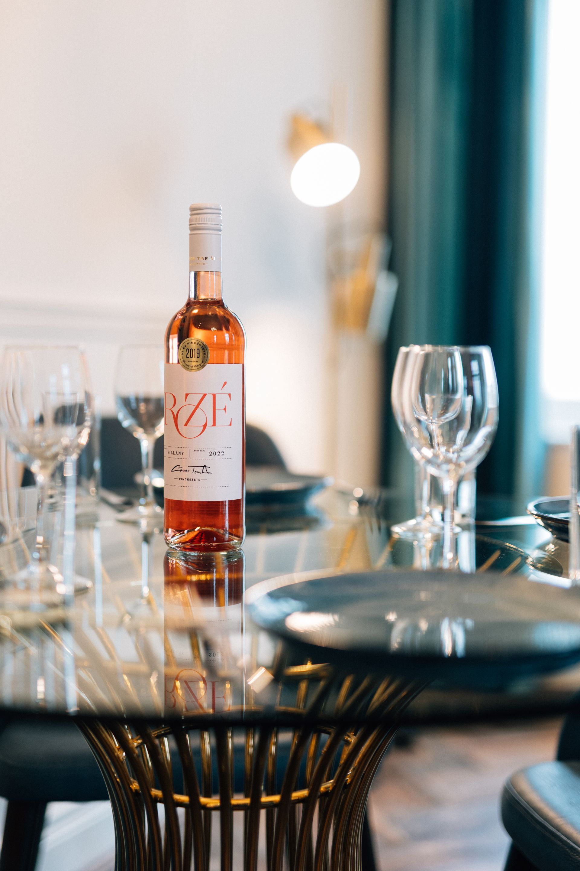 A bottle of rosé wine on a glass table set for a meal. 