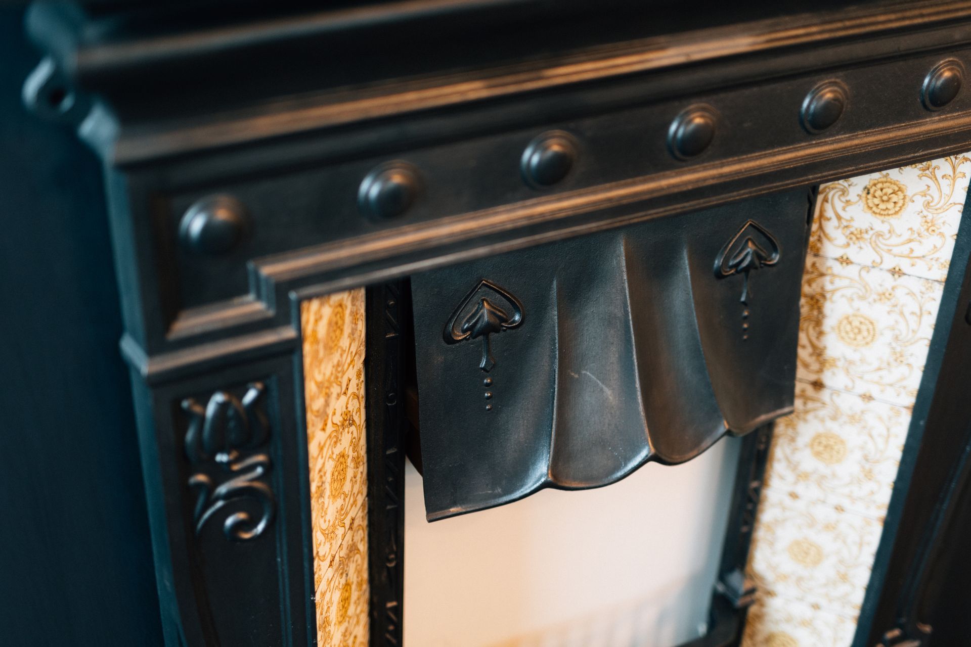 Close-up of a black antique fireplace mantel with decorative details. Gold patterned fabric accents the sides of the firebox.