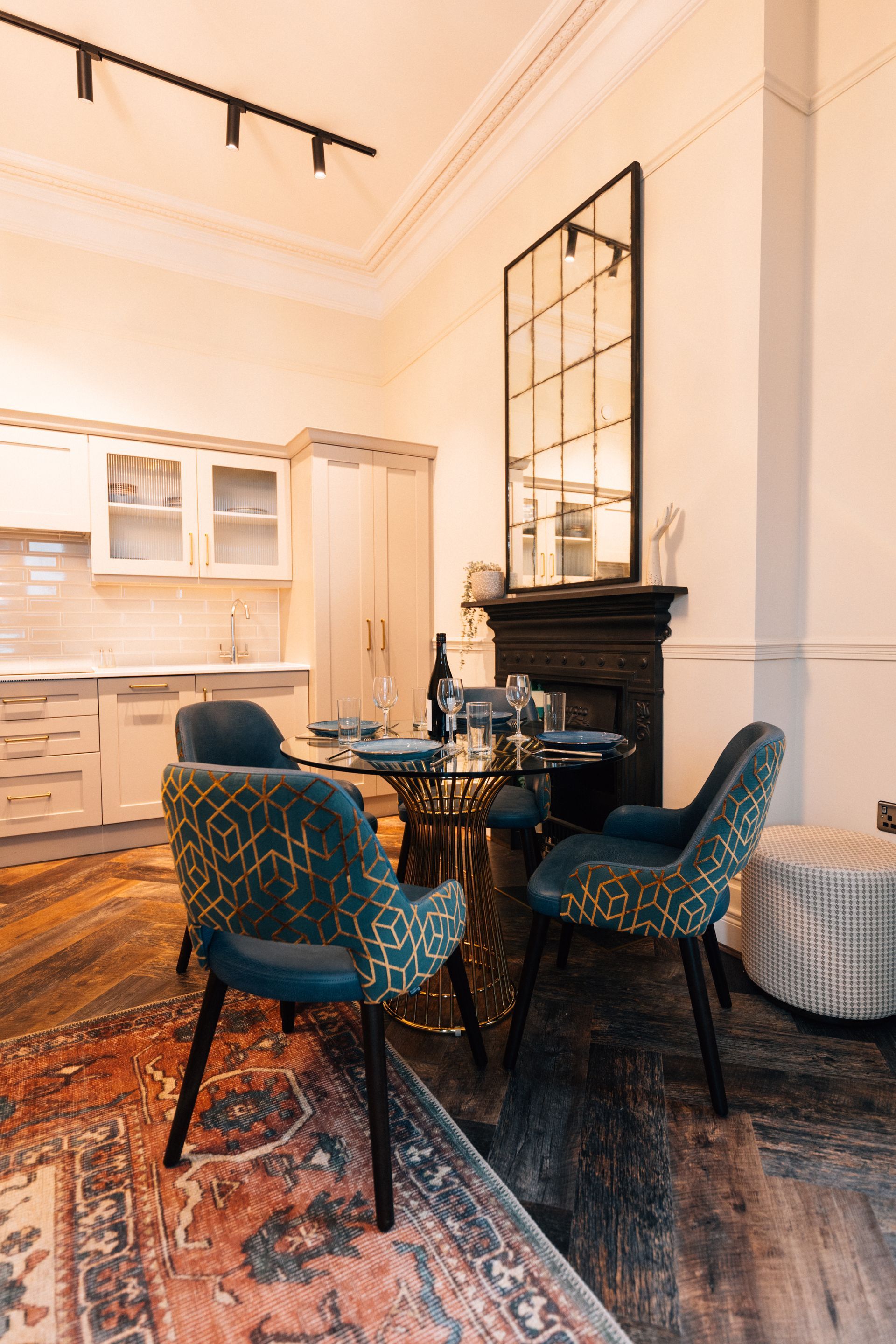 A dining area with a glass table, patterned chairs, and a large mirror above a fireplace. 