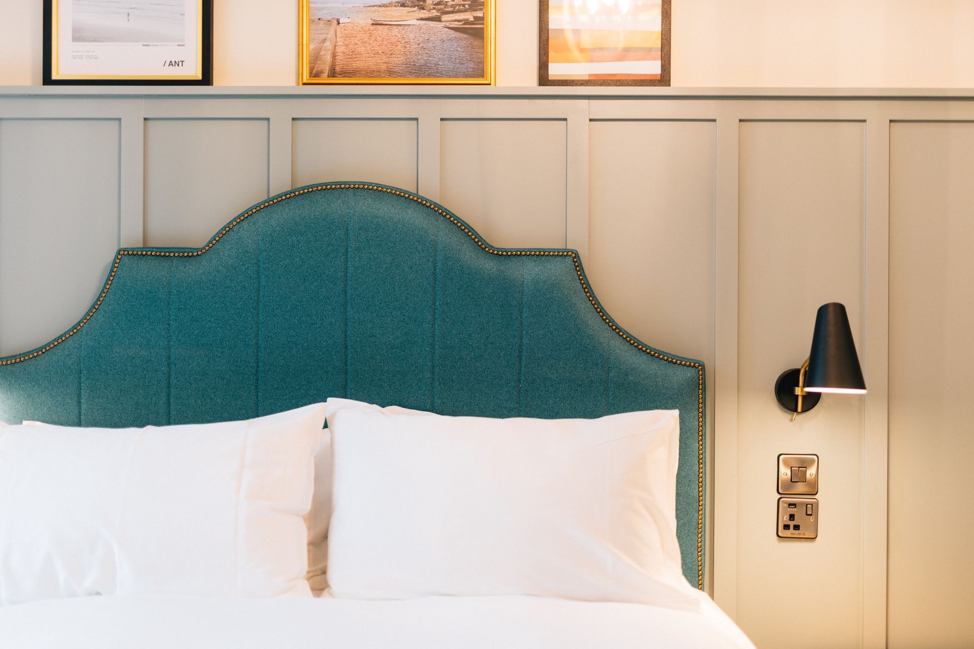 A bed with a teal headboard, white pillows, and a wall-mounted black lamp in a bedroom.