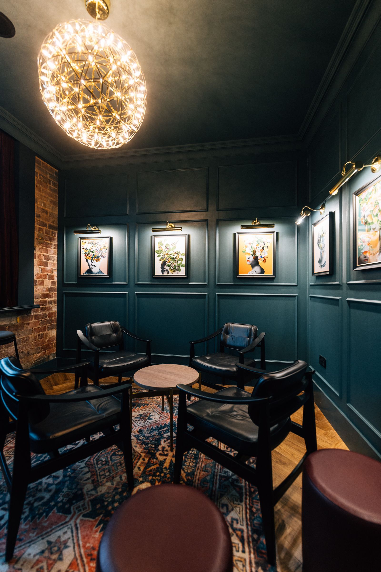 A cozy lounge area with dark teal paneling, black chairs, and artwork under warm lighting. 