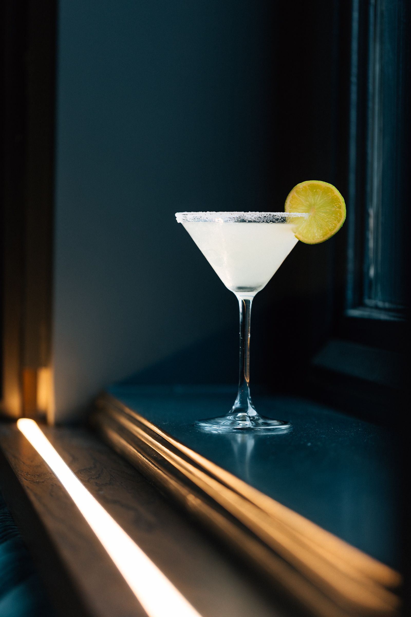 A classic margarita with a salt-rimmed glass, lemon slice, and a dark moody background.