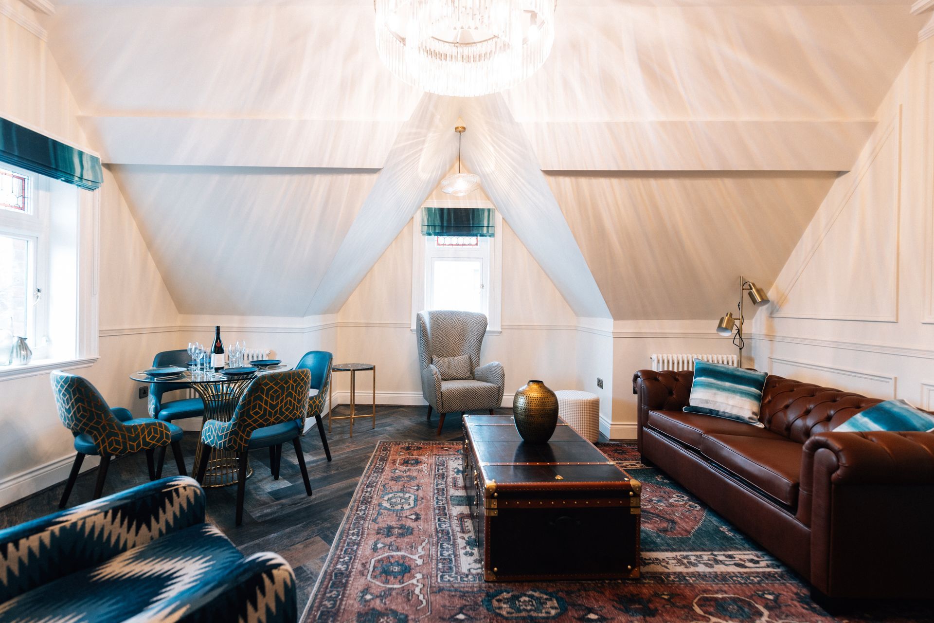 A living room with a leather sofa, patterned chairs, a dining table, and a patterned rug under a sloped ceiling.