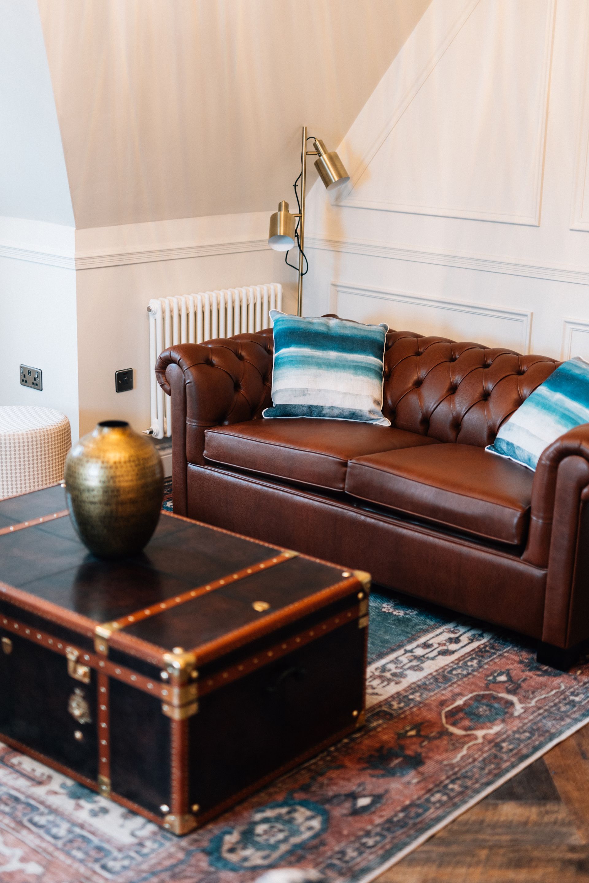 Brown leather couch with blue pillows and a trunk-style coffee table in a cozy living room setting.