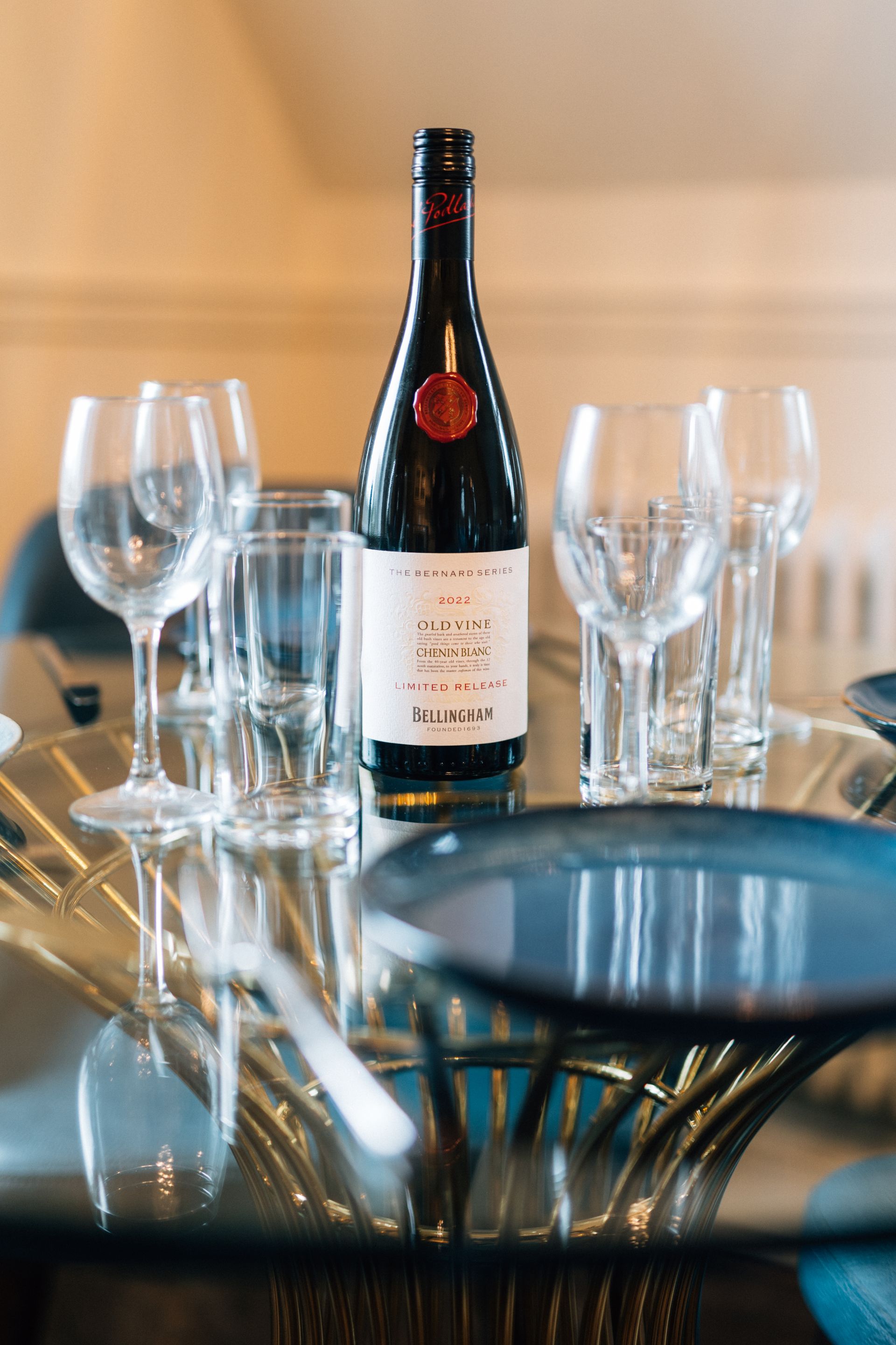 Wine bottle on a glass table set for a meal. Empty wine glasses and plates are visible.