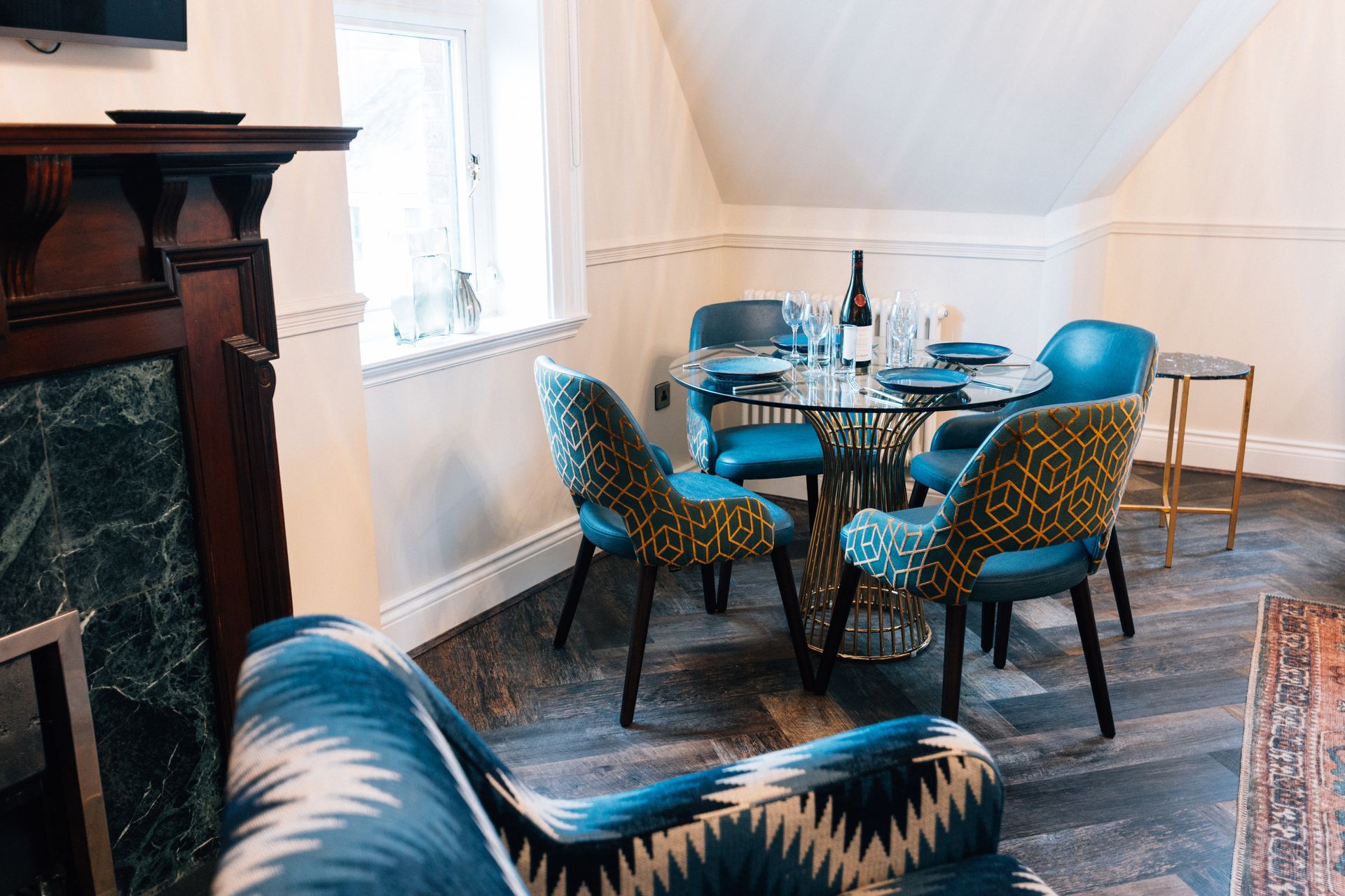 Cozy dining area with a round glass table set for a meal, surrounded by blue chairs with patterned backs,