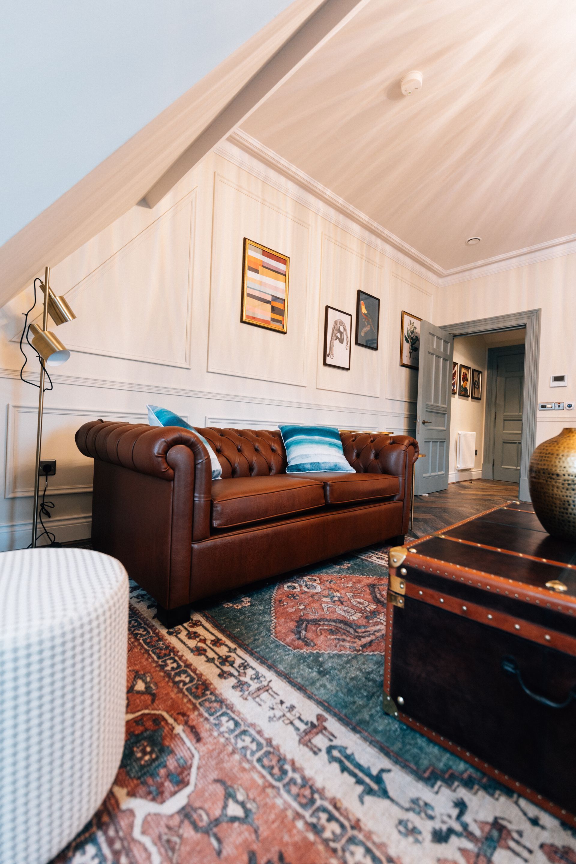 A living room with a brown leather Chesterfield sofa, a patterned rug, and a trunk used as a coffee table.