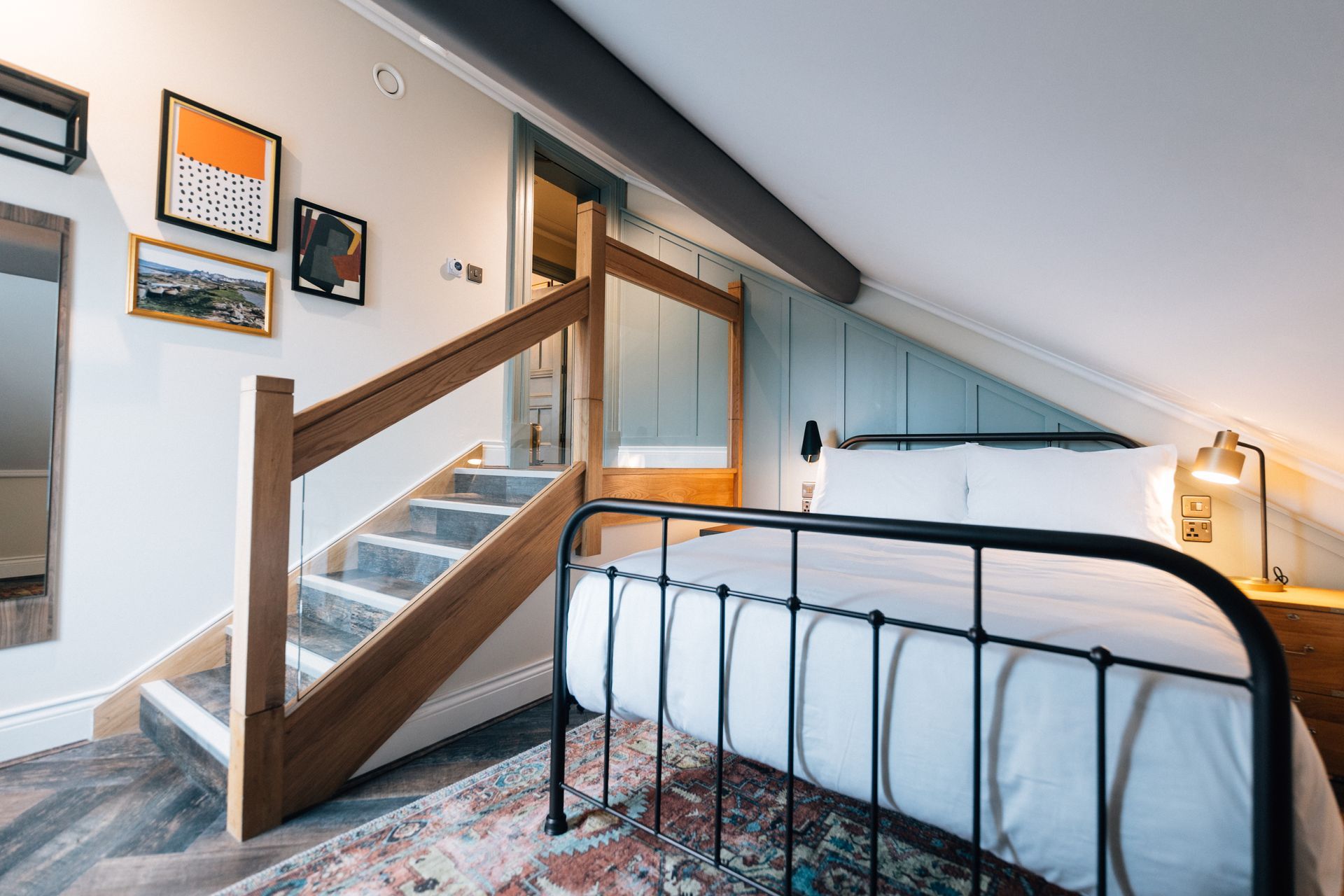 A bedroom with a bed, stairs, and artwork on the wall; light blue accent wall behind the bed, gray stairs.