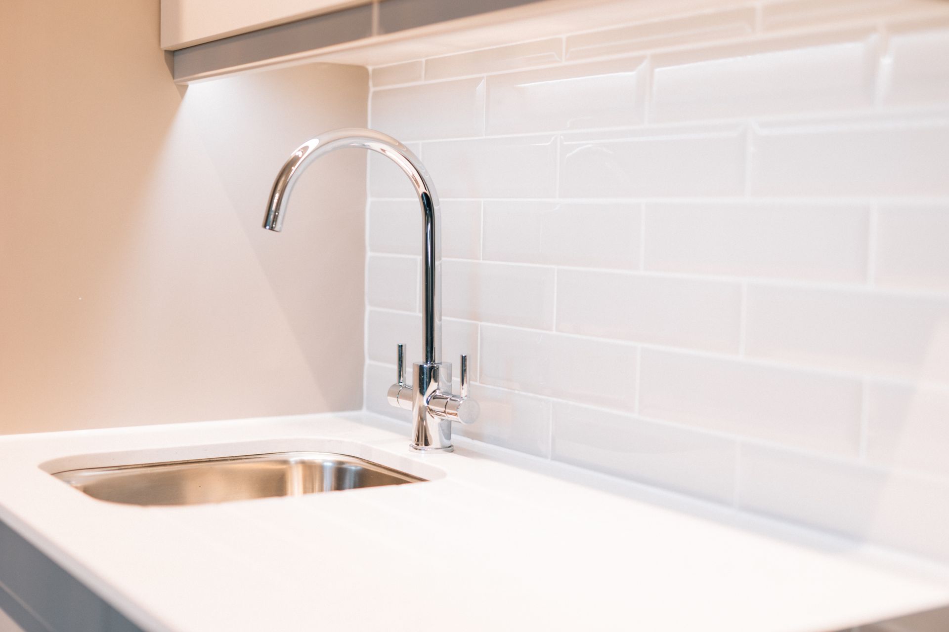 Stainless steel sink and faucet on a white countertop, with white subway tile backsplash and recessed lighting.