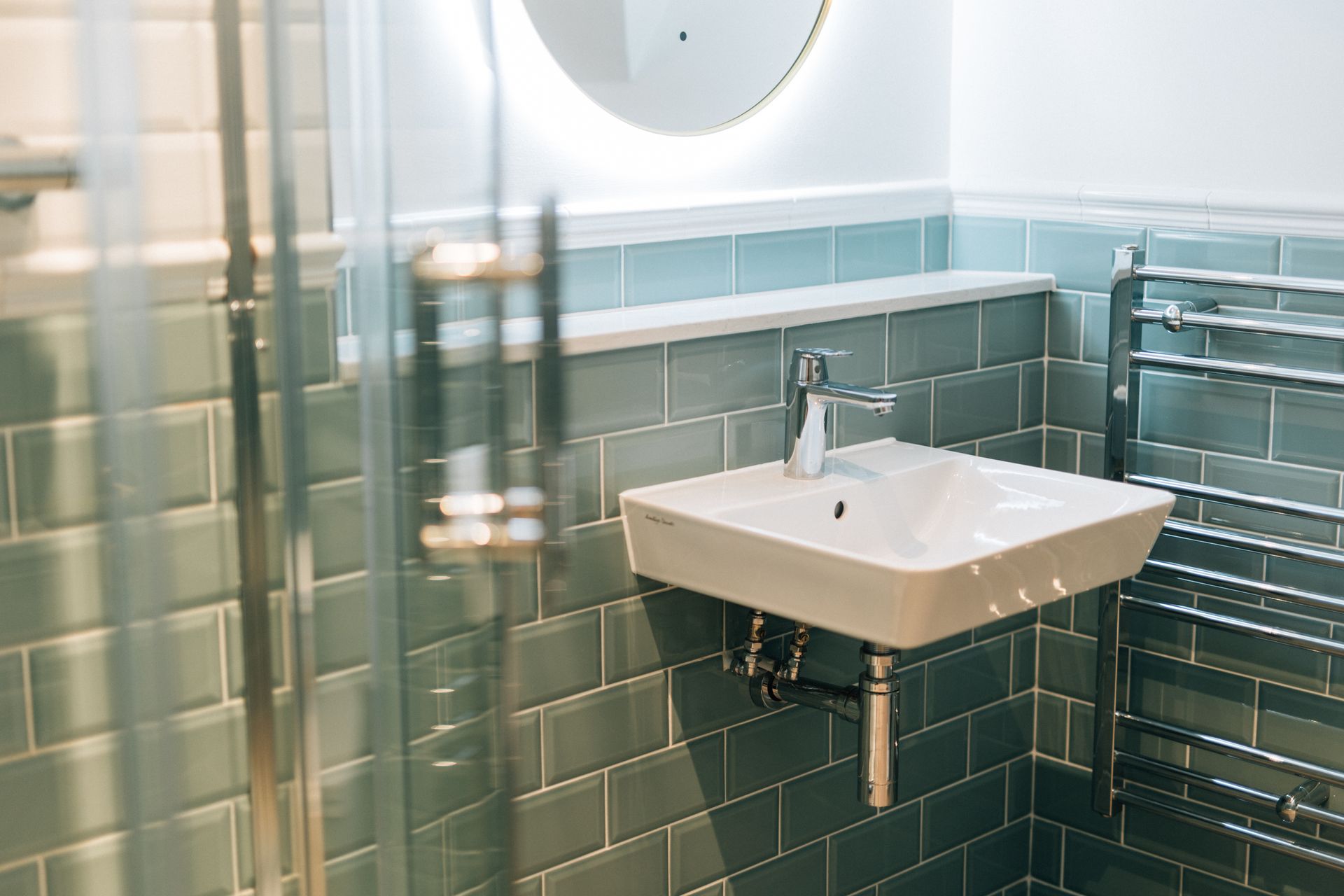 A modern bathroom with a square white sink, silver fixtures, and blue-green tiled walls. 