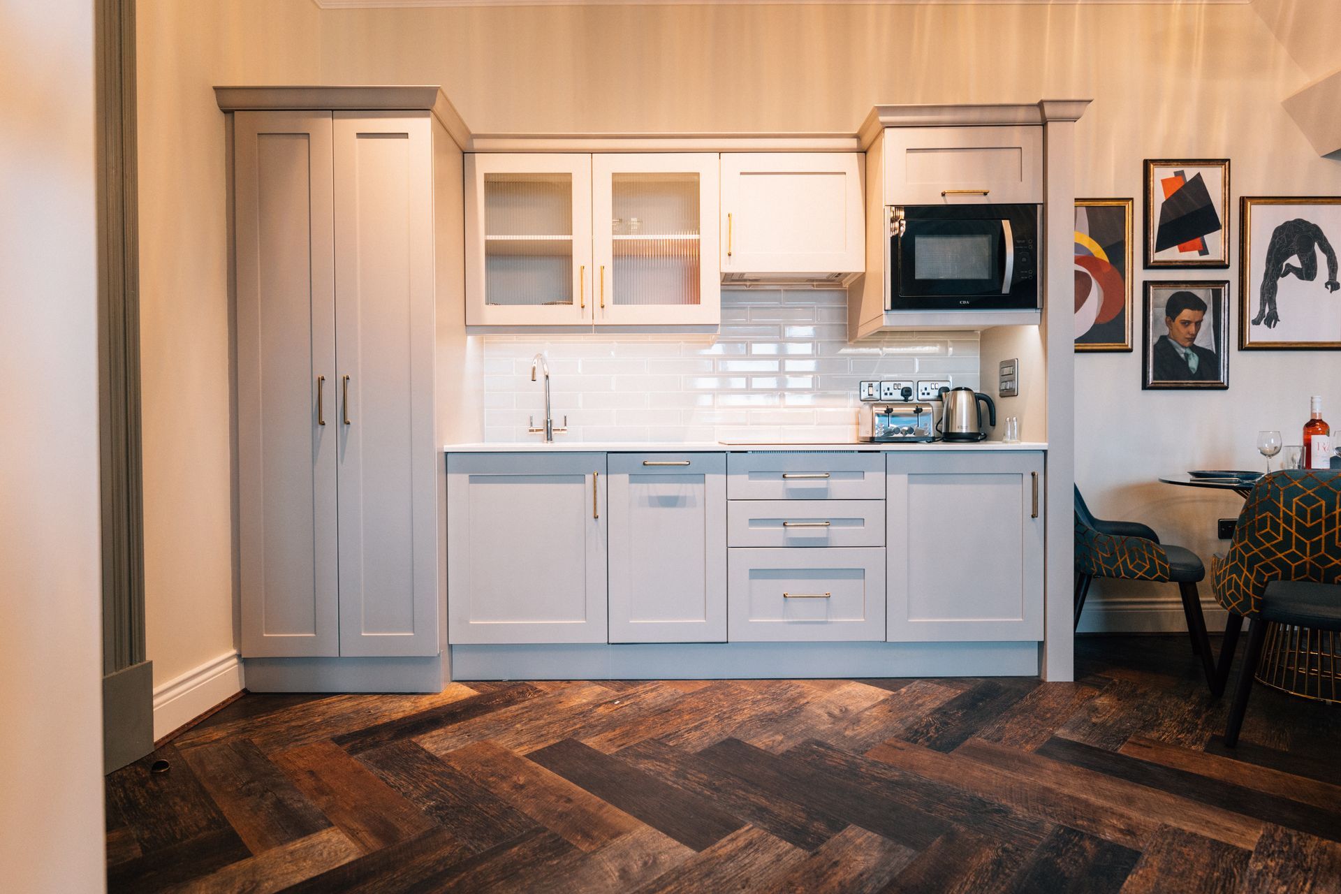 Small, modern kitchen with light gray cabinetsm, includes microwave, toaster, and artwork.