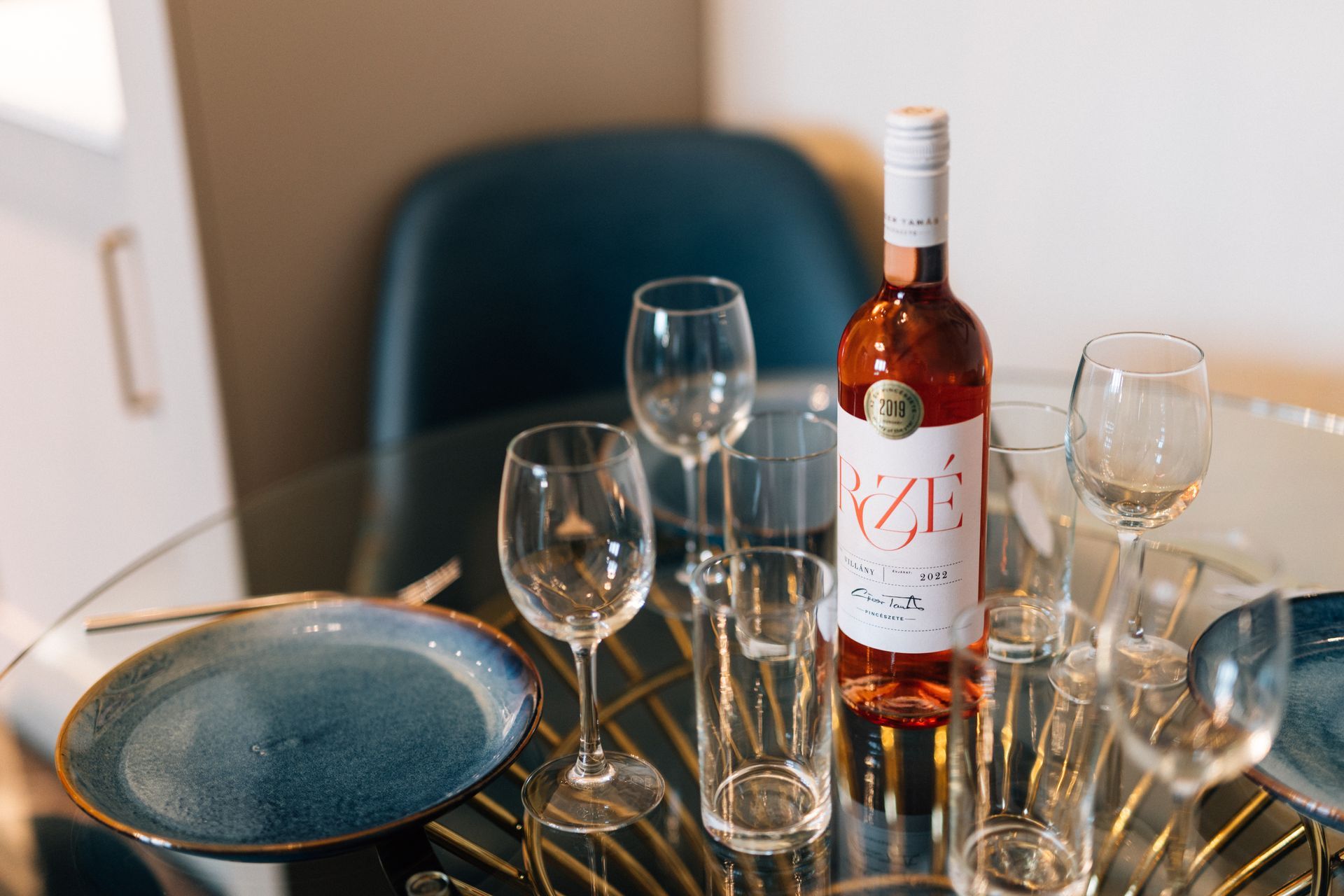 A table set for a meal with a bottle of rosé wine, plates, and glasses. 