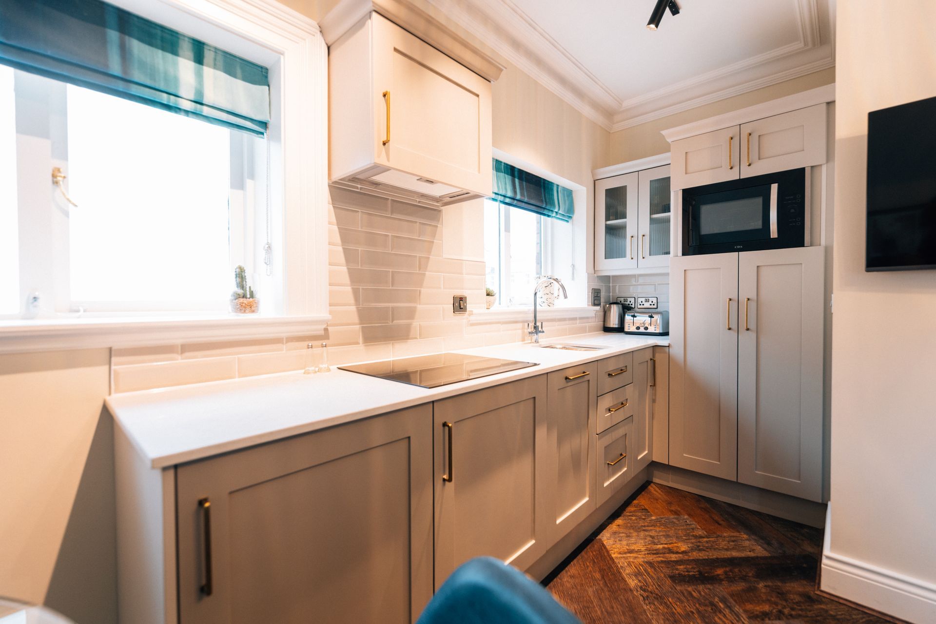 Small, light-toned kitchen with white countertops, light grey cabinets, and a microwave. 