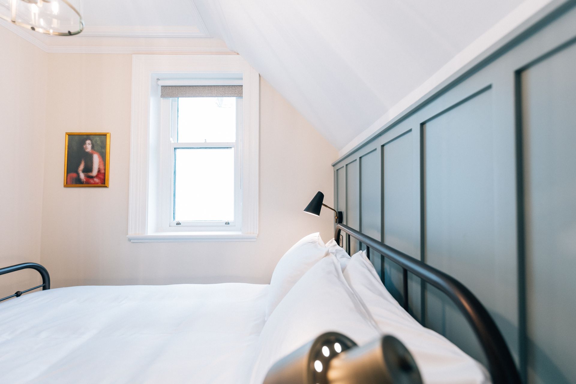 Bedroom with bed, window, artwork, and angled ceiling, painted in light and dark neutral tones.