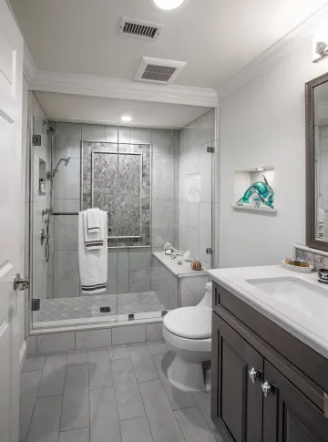 Bathroom with a walk-in shower, toilet, vanity, and a decorative alcove with a sculpture; light gray and white.