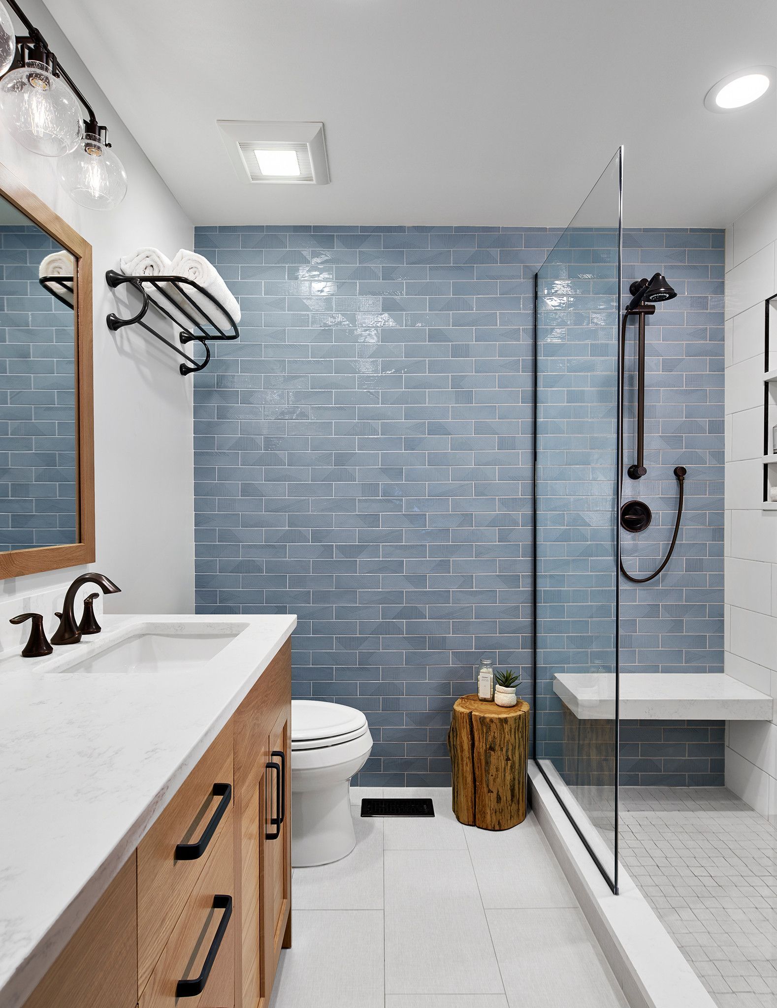 Modern bathroom with blue tiled shower, wood vanity, and glass shower door.