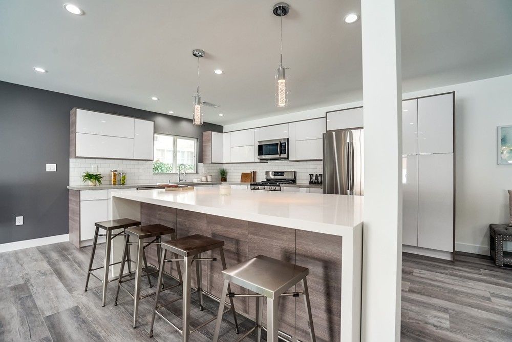 A kitchen with white cabinets , stainless steel appliances , a large island and stools.