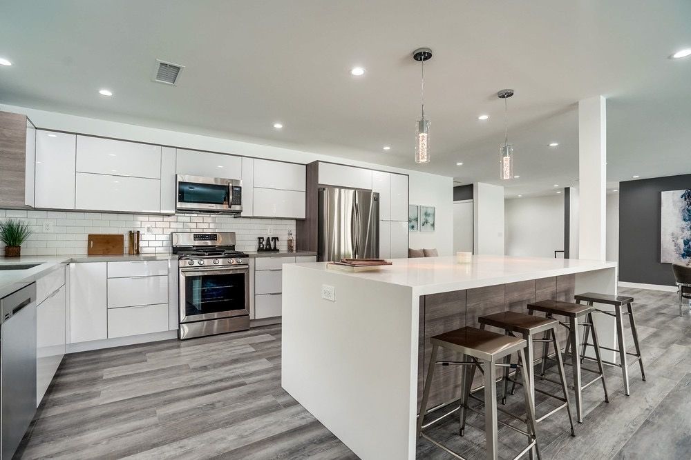 A kitchen with white cabinets , stainless steel appliances , a large island and stools.