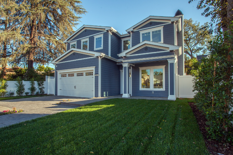 A large blue house with a white garage door is sitting on top of a lush green lawn.