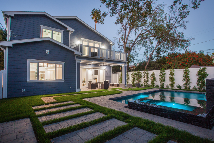 Blue house with a pool and patio at dusk.