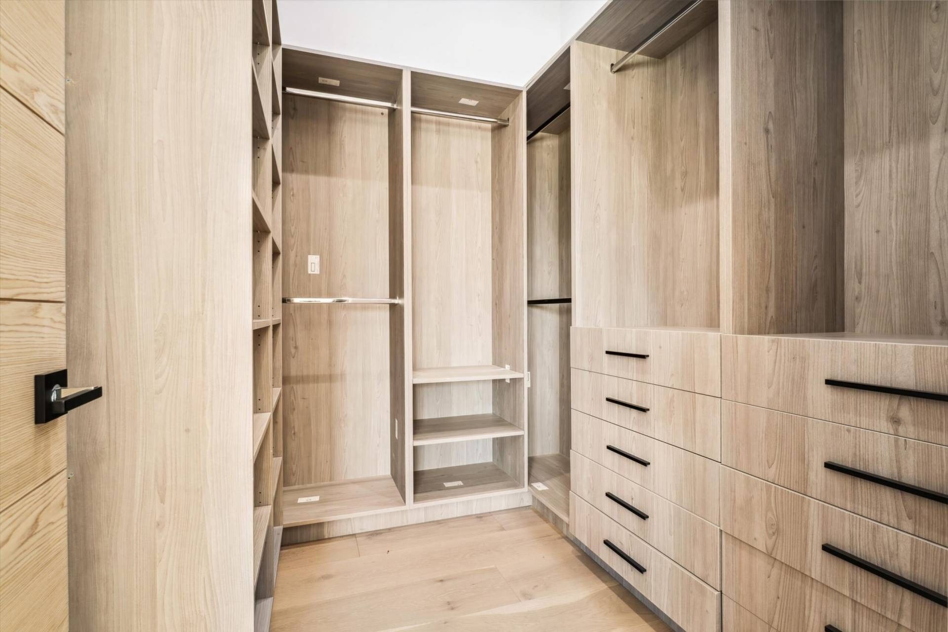 Empty, light-wood walk-in closet with shelves, drawers, and hanging rods. Modern design with neutral tones.