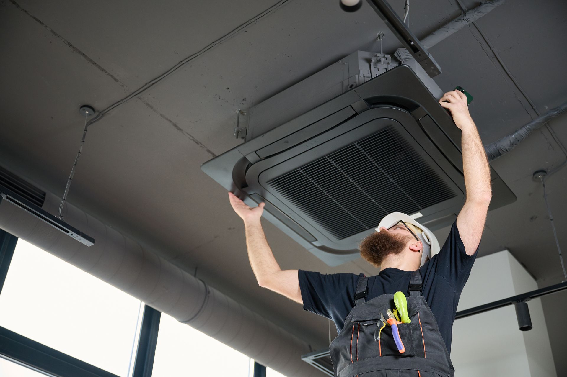 A professional installing an overhead air conditioning unit in an office building.