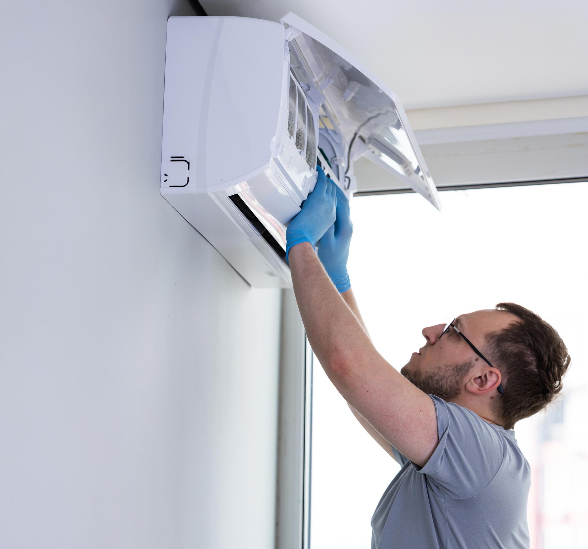 Side View of a male contractor as he checks on an AC unit with blue gloves.