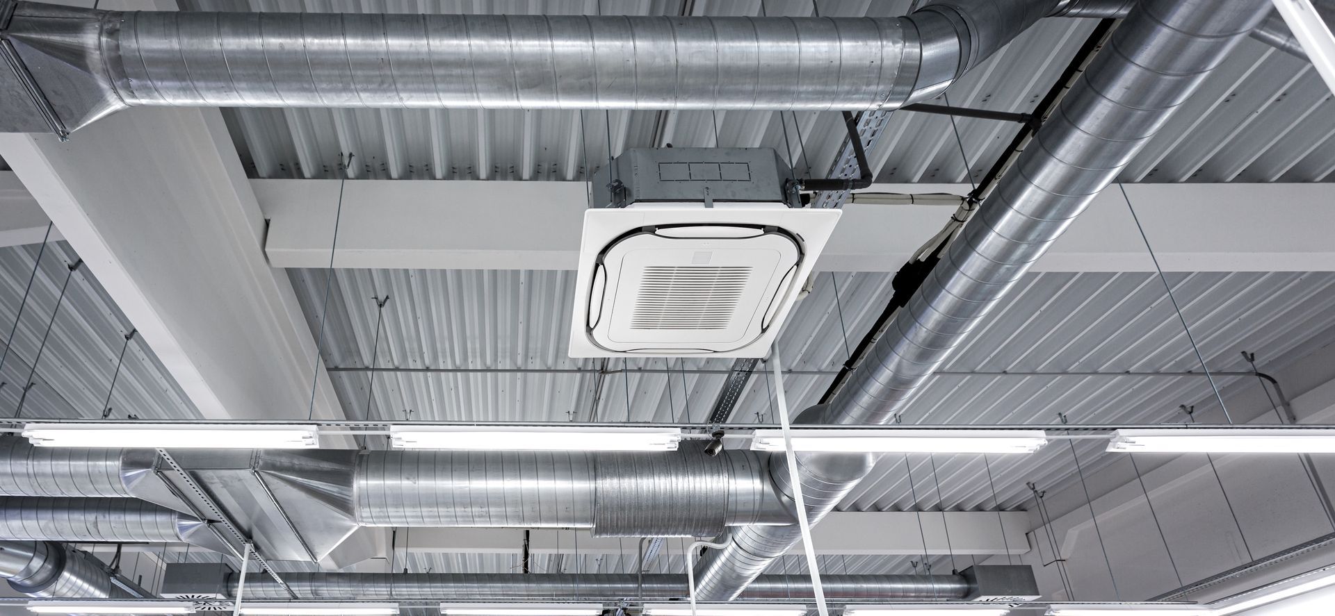 Ceiling-mounted commercial air conditioning system connected to exposed ductwork and vents.
