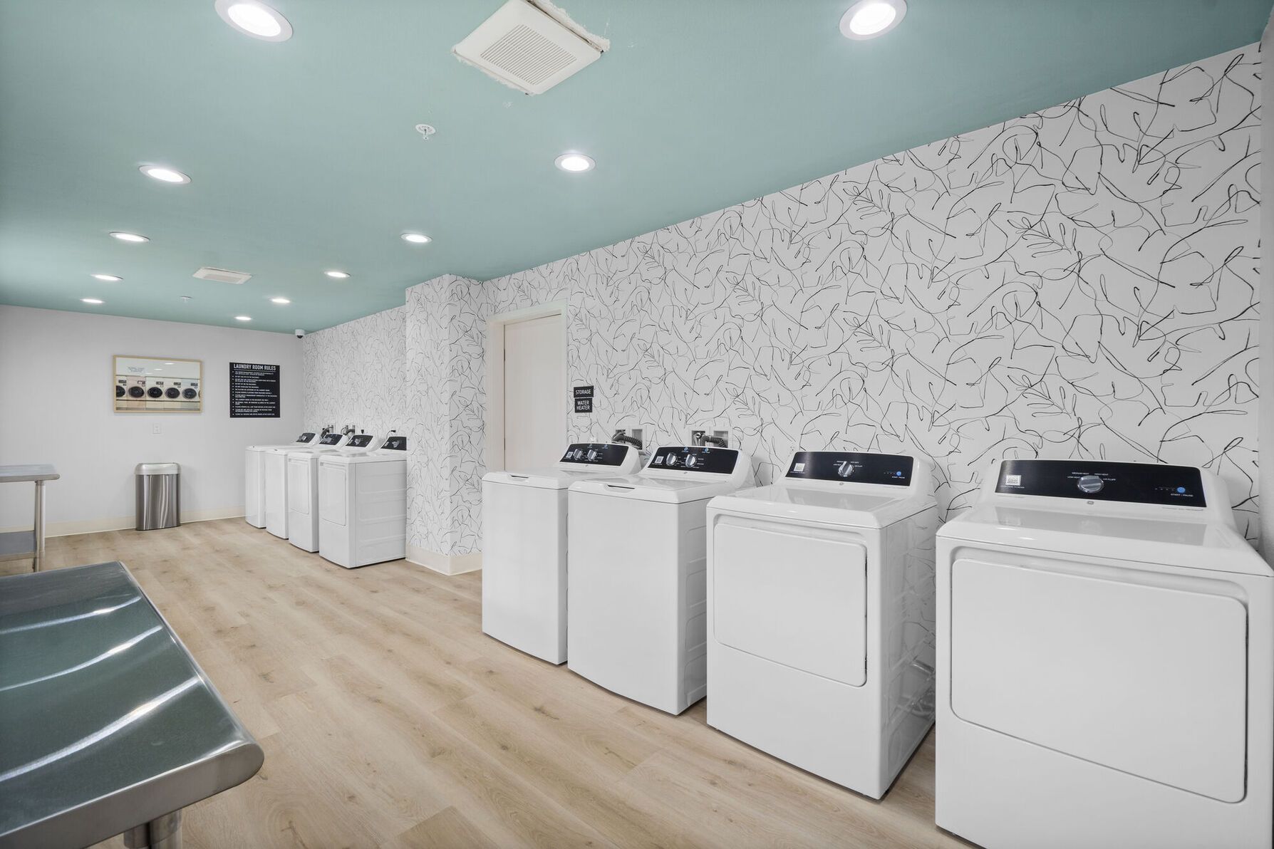 Photo of the laundry room, showing several washers and dryers, as well as a couple of folding tables