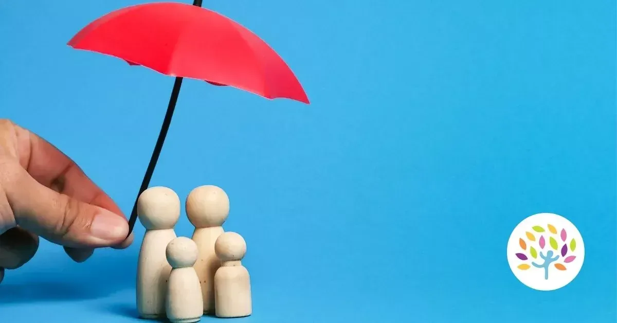 Hand holding a red umbrella over three wooden figures on a blue background