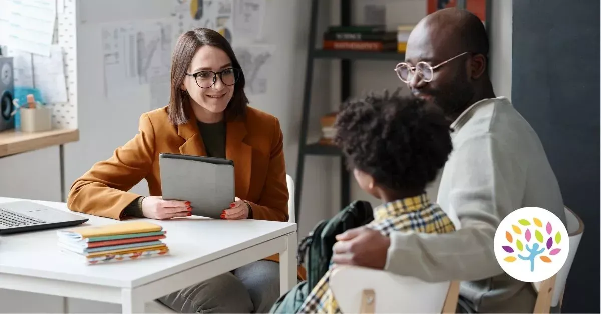Three people meeting at a table with a laptop and notebooks in a bright office