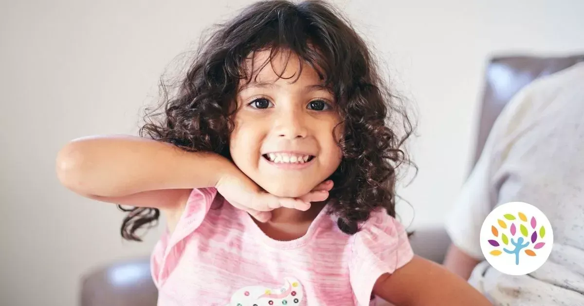 Smiling child in a pink shirt making a playful pose indoors