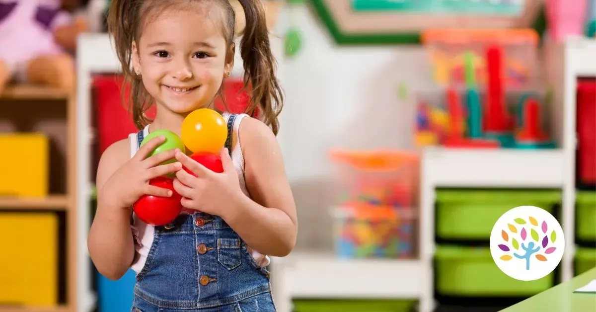 Smiling child holding colorful toy balls in a bright playroom
