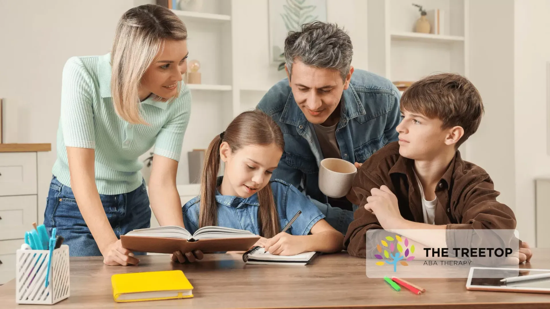 A family sits together at a wooden table in a bright room, helping children with their studies and writing in a book.